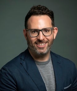 A man in a dark jacket smiles at the camera.