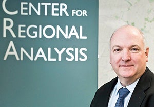 A man in front of a Center for Regional Analysis sign in a suit and tie looks at the camera.