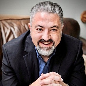 A man in a dark jacket and silver hair smiles at the camera.