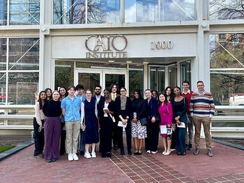 A group of well-dressed people stand in front of a glass and chrome building.