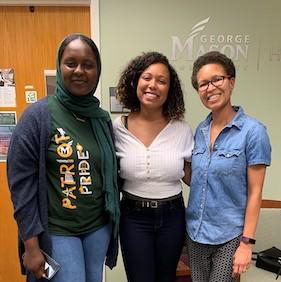 Three women smile for the camera in the office of fellowships at George Mason University