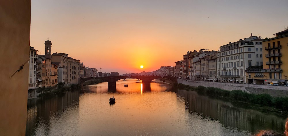 Sunset over the water and a bridge of a European city. Buildings line the borders of the water. 