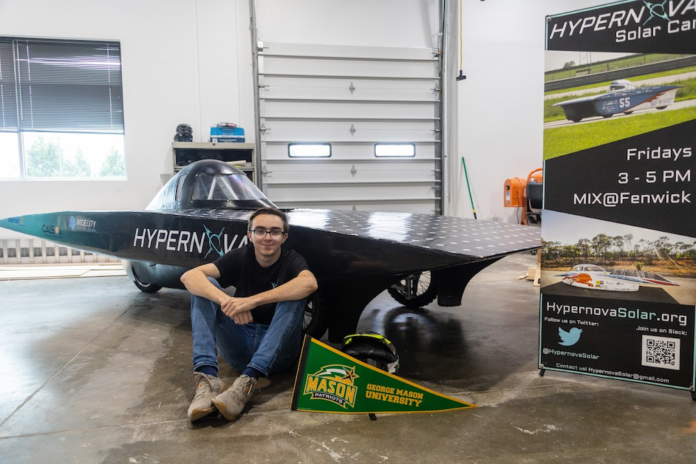 George Mason student Michael Riggi sits in front of a black solar car that his student team at Mason, Hypernova Solar, helped revamp.