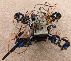 A black mechanical robotic spider with colorful electrical wires is presented as an example of a hardware project students might create at the HackOverFlow hackathon.