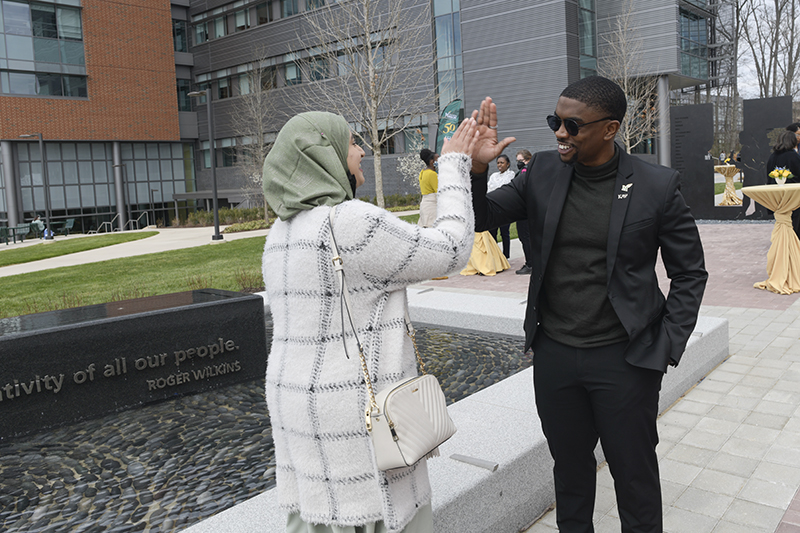 Ayman Fatima and Kye Farrow give each other a high-five next to the Enslaved People of George Mason Memorial at the memorial dedication