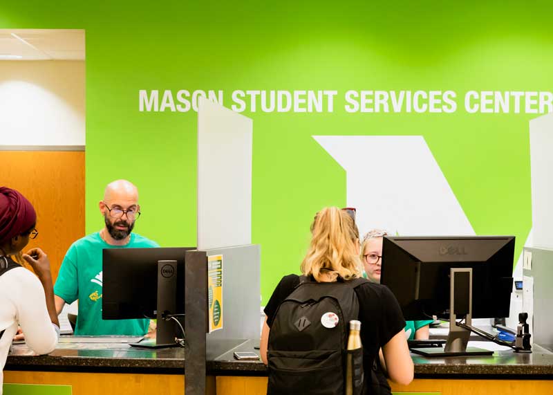 Students consult with MSSC personnel at the customer service desk. The desk resembles a long bank counter with privacy partitions between each service window. Personnel are attentive and friendly. Students appear relaxed. 