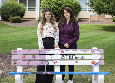 two women standing by a decorated bench
