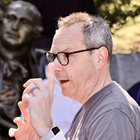 A man in glasses stands in profile with a statue behind him.