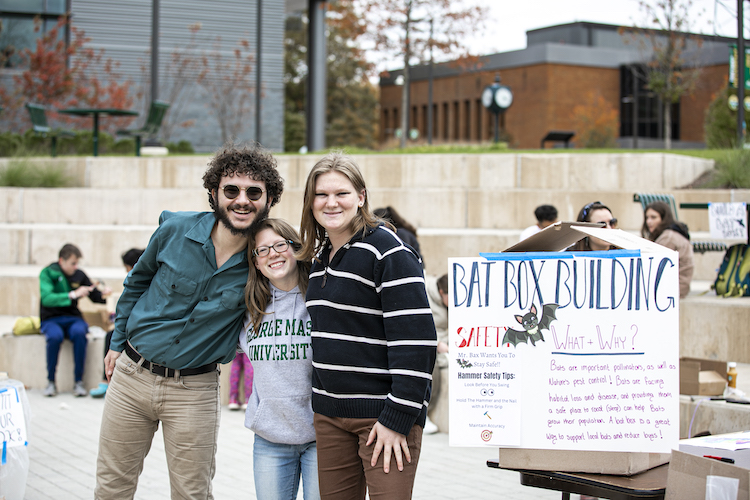 three students with sign on Wilkins Plaza