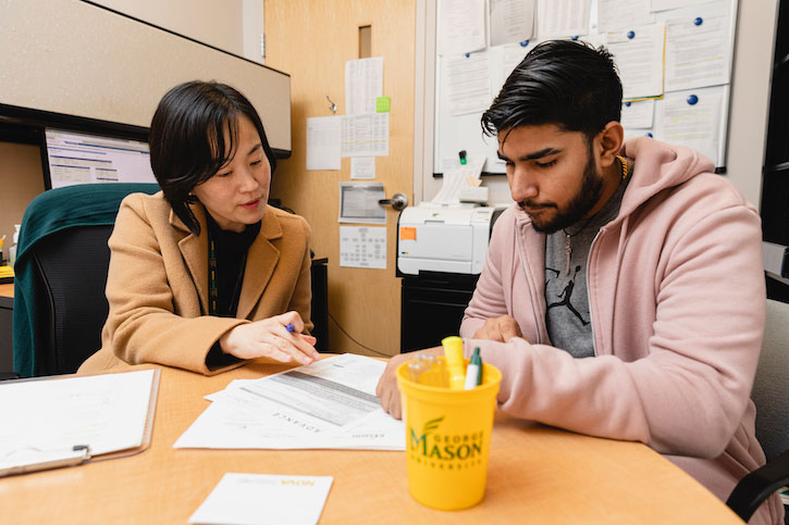 Sharon Kim assists a student with the transfer process in the ADVANCE program. They sit focused on paperwork at a round table in an office environment