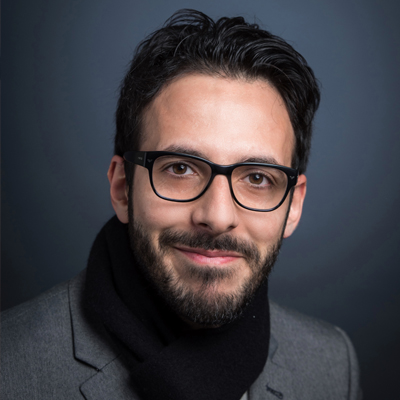 Pouyan Ahmadi wears a gray blazer, black scarf, and glasses in his faculty profile for the IST department at George Mason University.
