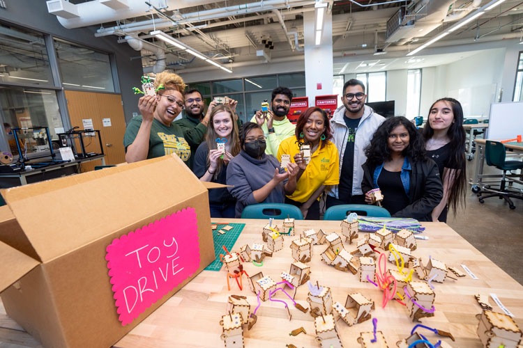 A diverse group of students, faculty, and staff at Mason hold up wooden toys they built for a toy drive