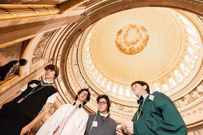 Young people with tourist headphones stand under an ornate gold dome.