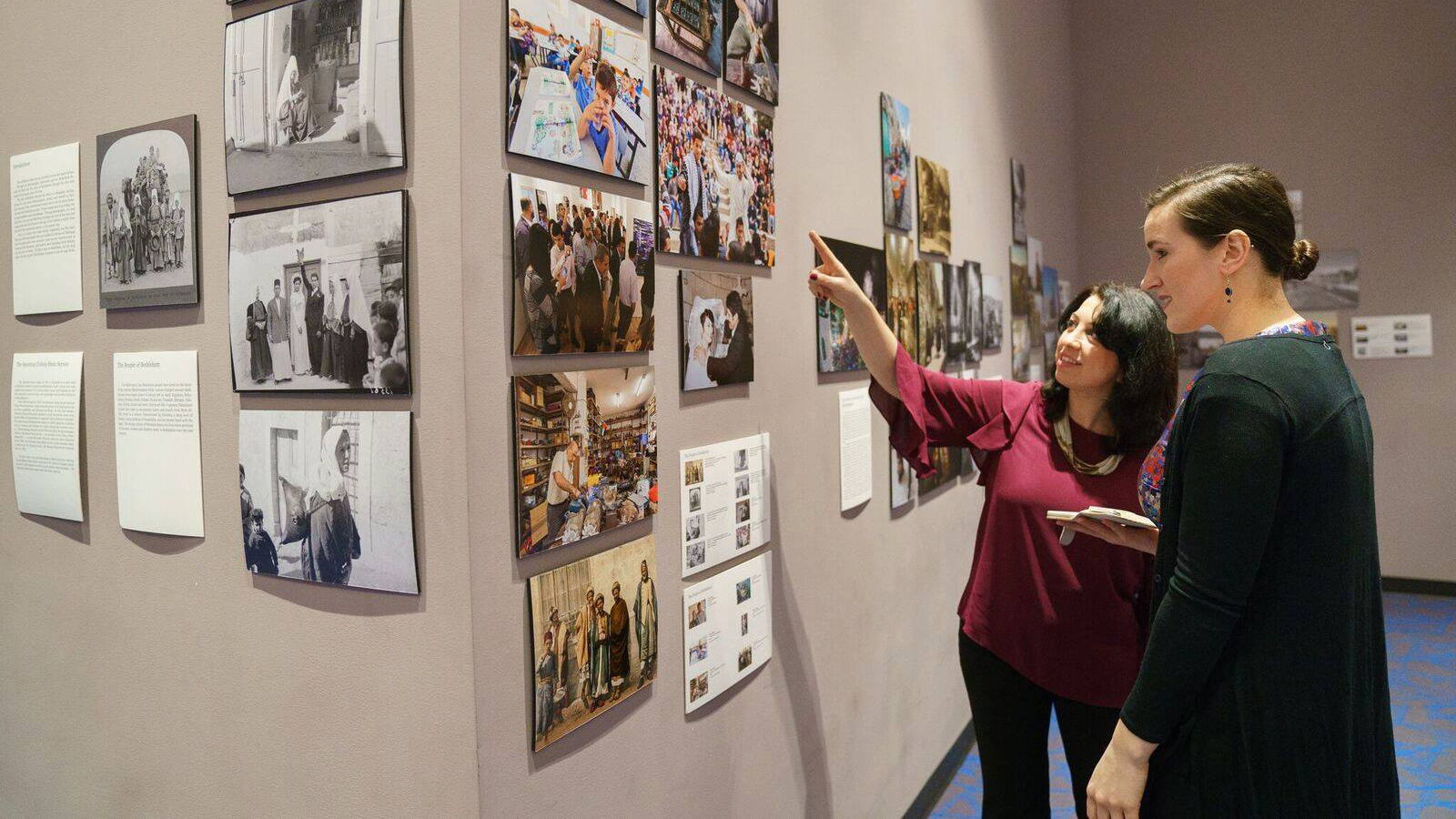 Fakhira Halloun shows a guest around the Museum of the Palestinian People. Her arm is raised pointing to photos on a wall.