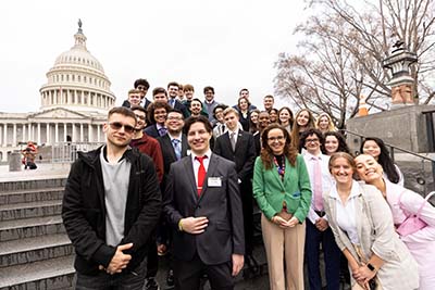 A group of well-dressed students and their teacher pose in front of the Capitol building.