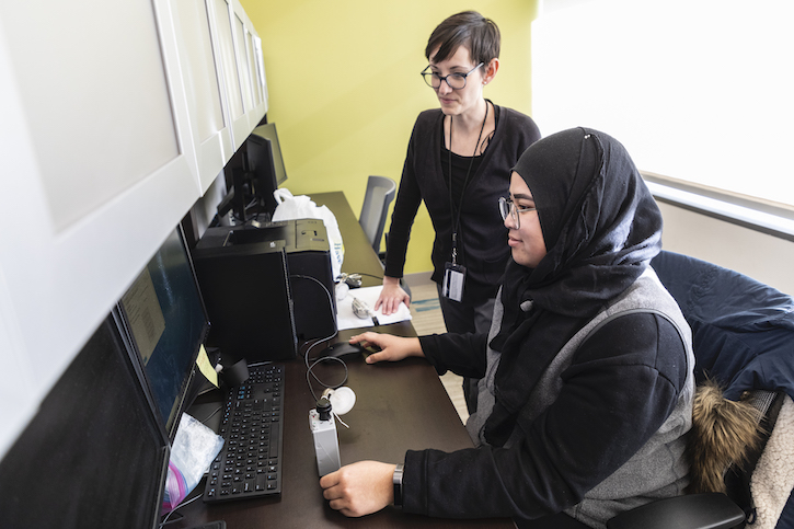 Nadia Abidah downloading data from an air pollution monitor at a computer. Dr. Jenna Krall is looking over her shoulder at the computer monitor.