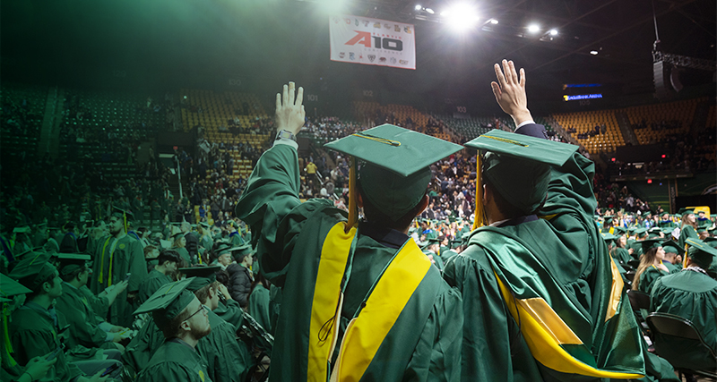 A pair of graduating students wave to a crowd in EagleBank Arena 