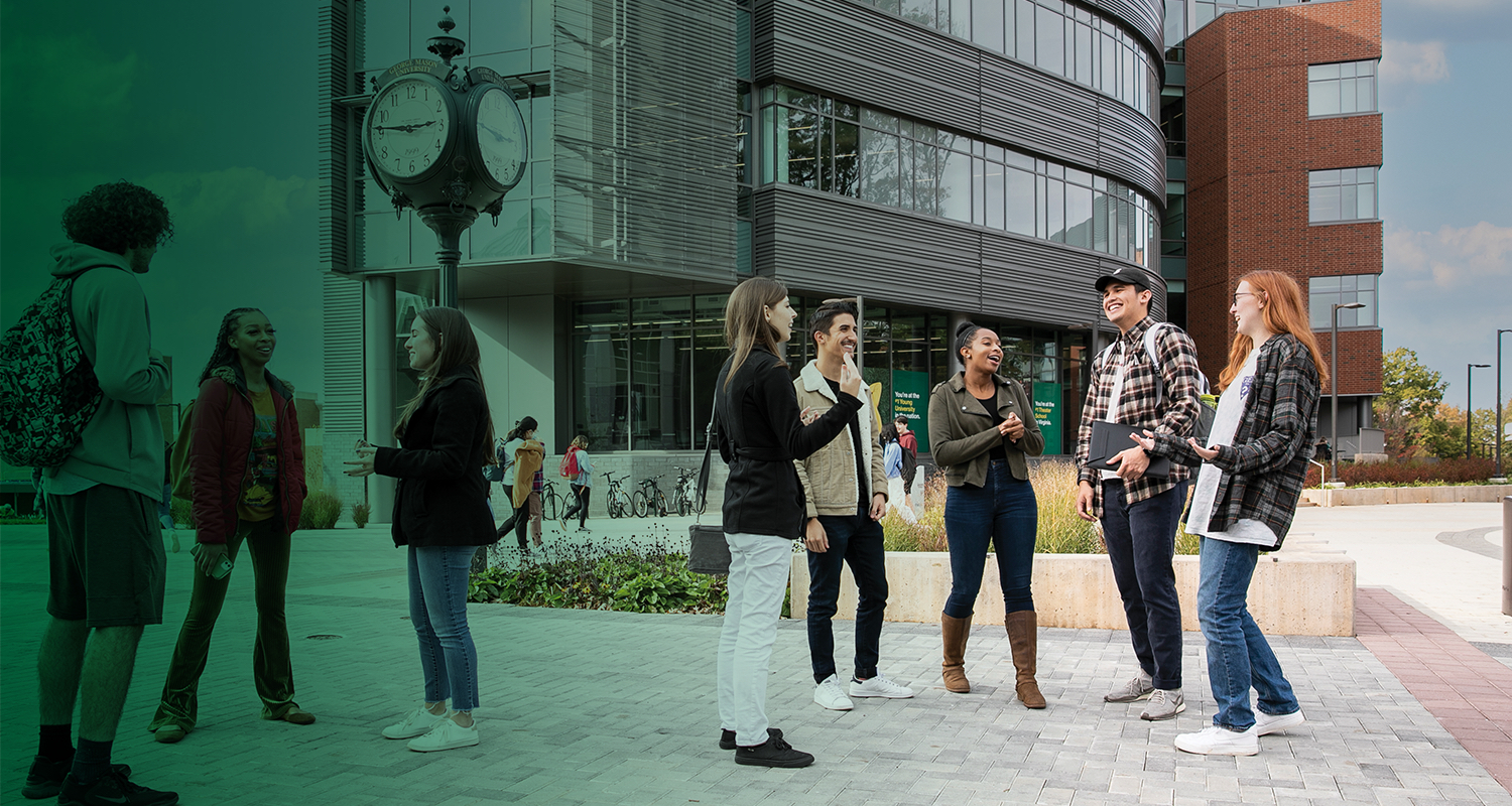 A group of Mason students converse around the clock in the center of Wilkins Plaza.