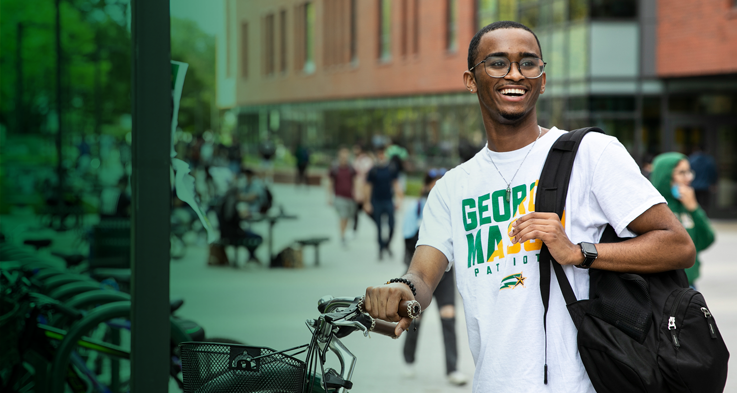 A Mason student stands next to a bike rack in Wilkins Plaza on the Fairfax Campus and smiles.