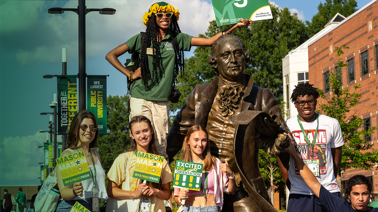 A group of incoming freshman and transfer students celebrate at the George Mason statue during their orientation.