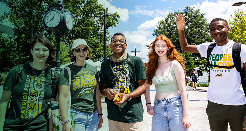 A group of diverse Mason students stand together smiling and waving in Wilkins Plaza on the Fairfax Campus.