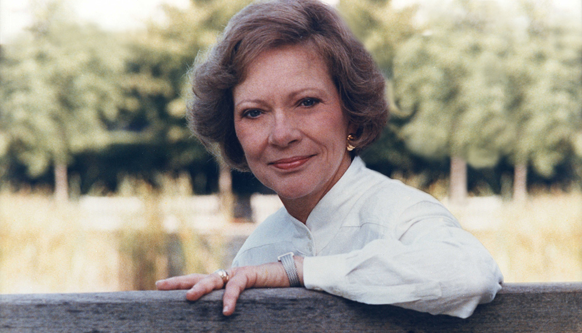 Rosalynn Carter seated outside turning to face the camera with trees in the background