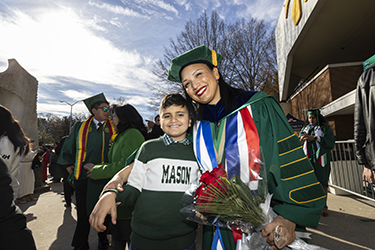 A graduate poses with her son while holding flowers.
