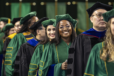 Doctoral candidates and their faculty advisors stand in line as they process into the EagleBank Arena.