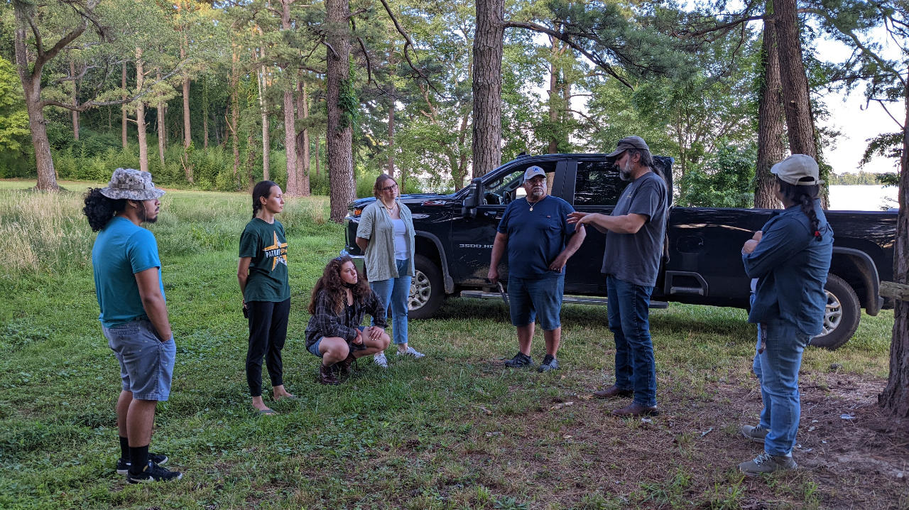 The Mason team standing with Dana Adkins of the Chickahominy Tribe during a wildlife assessment. They are outdoors and standing in a semi-circle.