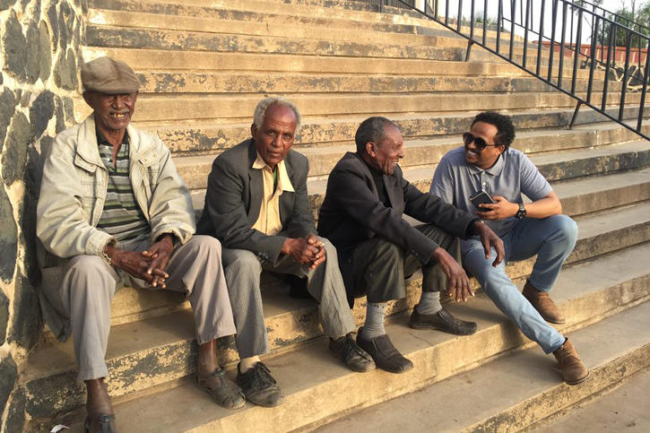 S-CAR Ph.D. student Felegebirhan Mihret sitting on steps and chatting with a group of local men in Asmara. 