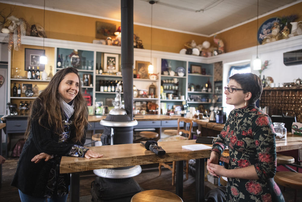 Junior Maya Prestipino (right) and Susan Leopold lean on a table at the apothecary and talk about wild ginseng.