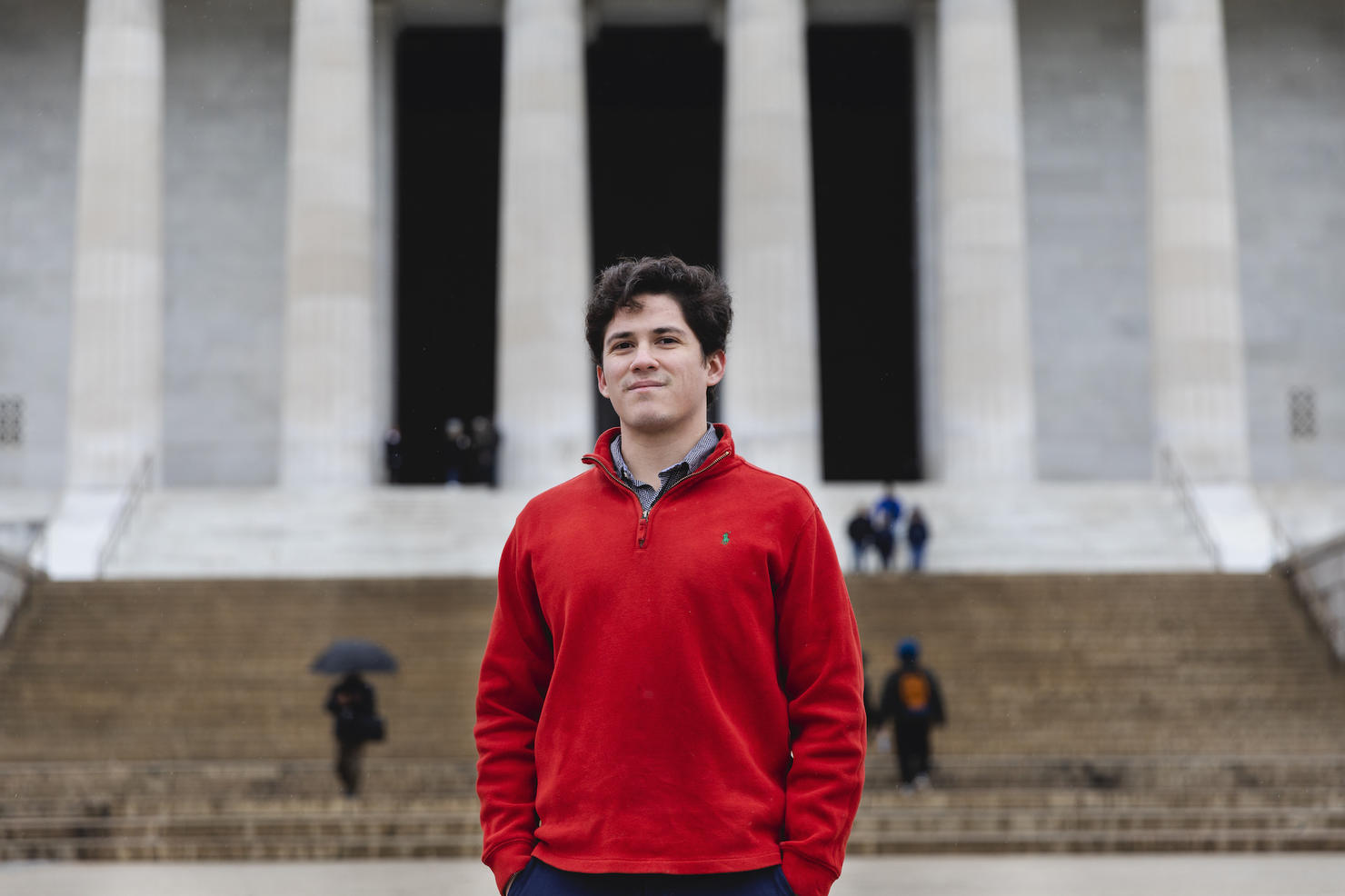 Yasser Aburdene standing on the steps in front of the Lincoln Memorial in Washington, D.C. His hands are in his pockets and he is wearing a red seater.