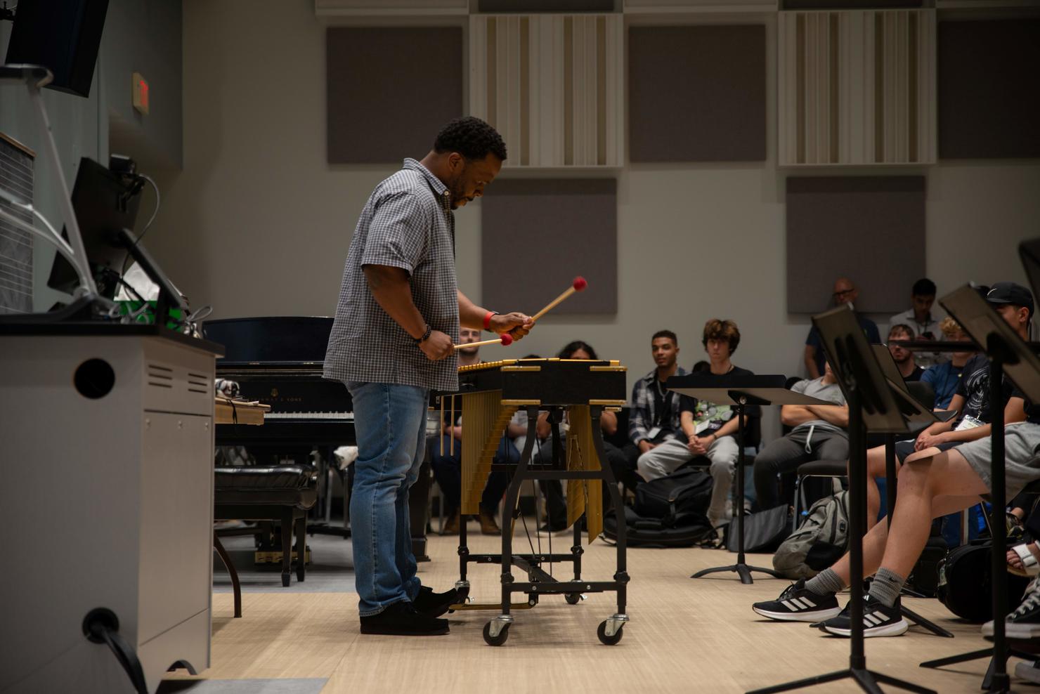 Special guest artist Warren Wolf teaches a masterclass to campers at Mason Jazz Camp in a music rehearsal room. He plays the vibraphone for students