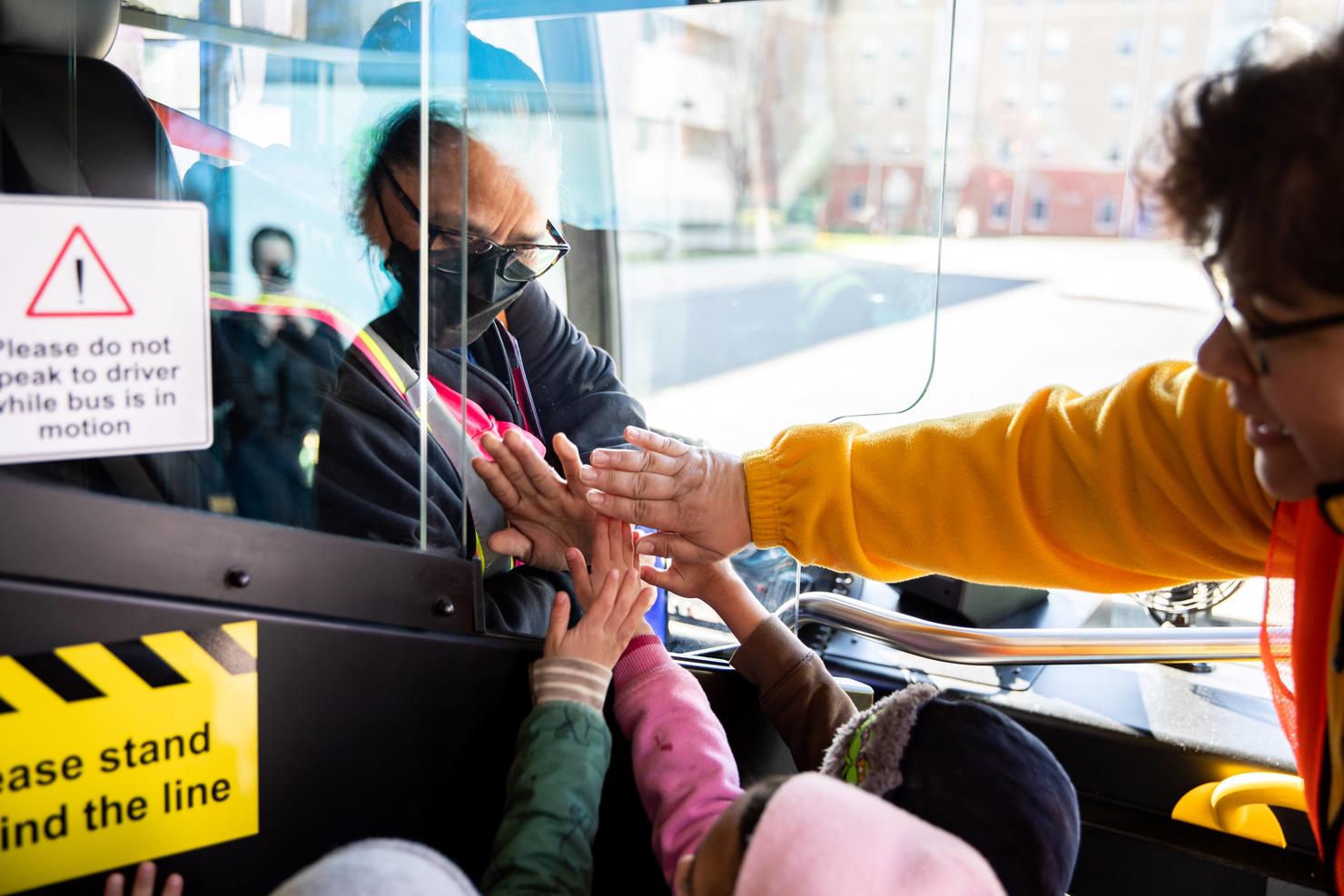 Young children touch hands with the bus driver through the partition