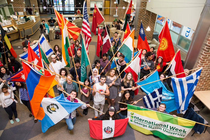 Students march at a parade in front of various international flags