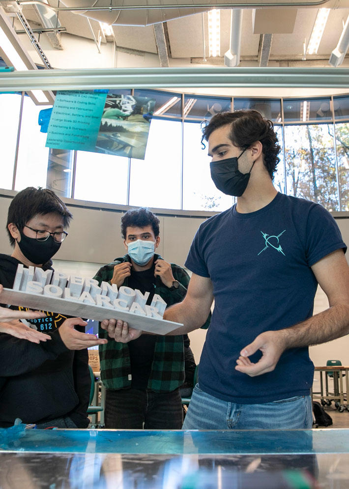Members of the Hypernova Solar Car Team work with a 3-D printed sign in the lab on the Mason Fairfax Campus