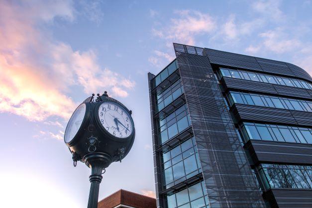 Looking up at the clock on Wilkins Plaza with a sunset sky and Horizon Hall in the background.