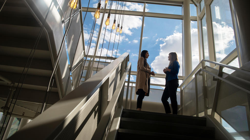 Two women stand talking in a sunny stairwell at an event with the Mary Hoch Center for Reconciliation.