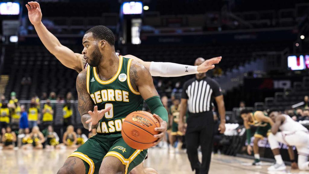 GMU basketball player on the court with the ball, blocking another player. The ref is on the right side of the photo.