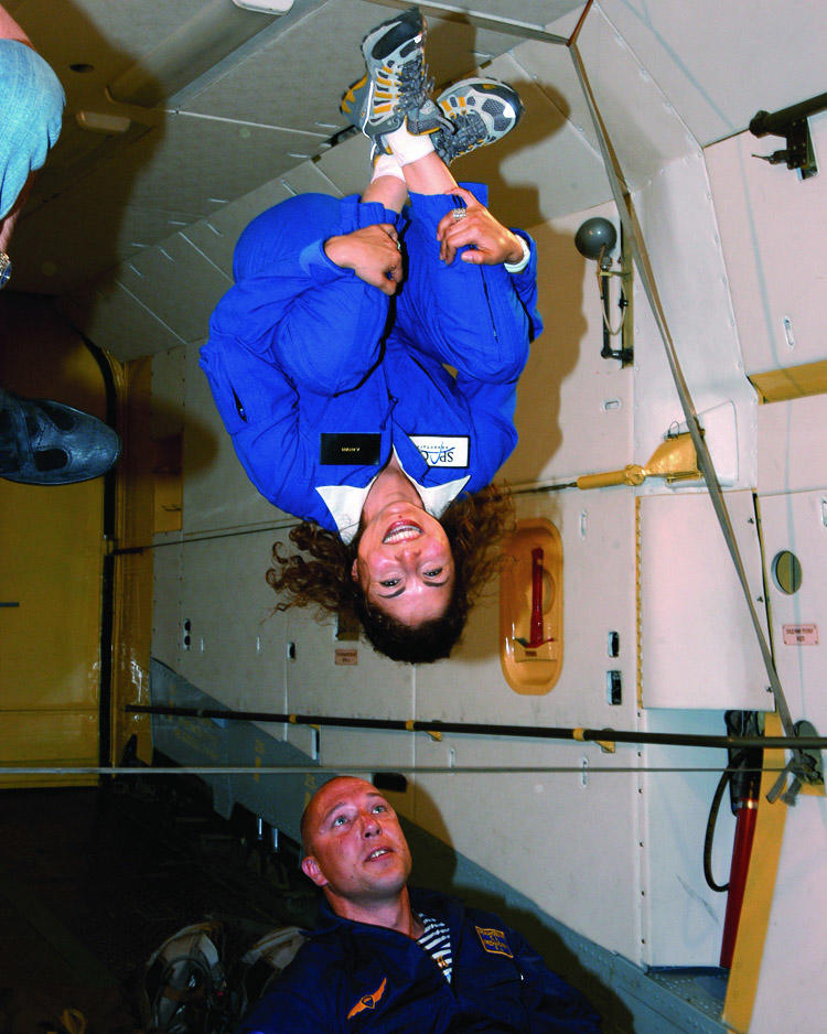 alum Anousheh Ansari wearing a bright blue one-piece is upside down in a spacecraft