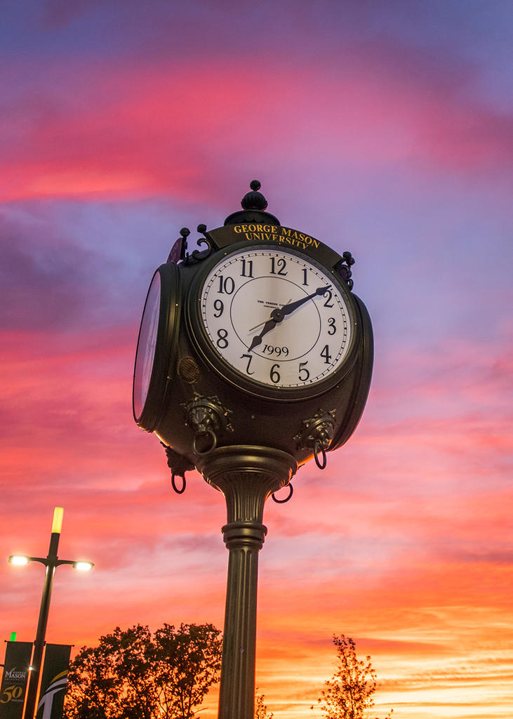 The clock in the center of Wilkins Plaza is backdropped by a sunset, turning the sky waves of purple, orange, and pink.