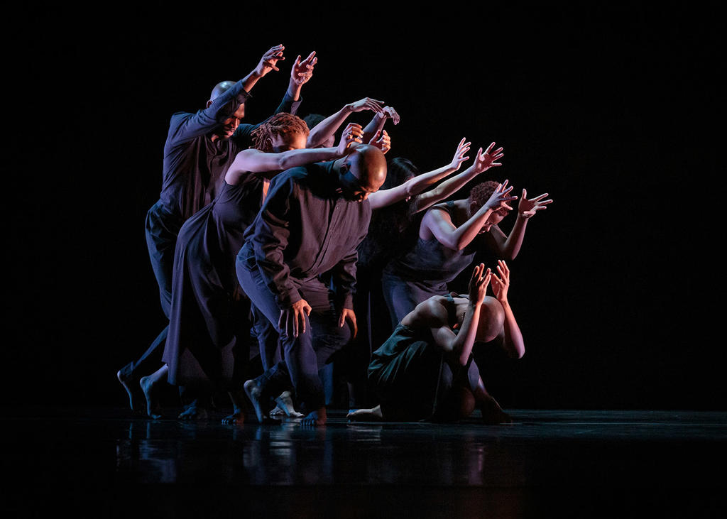 A group of dancers dressed in black lean towards the right with their arms outstretched while performing A.I.M by Kyle Abraham at Mason's Center for the Arts. 