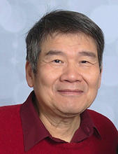 A head and shoulders portrait of Jeng Eng Lin in a red sweater, dark red collared shirt against a blue backgroung