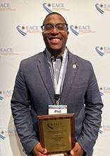 Philip Wilkerson III displays his award while standing in front of an EACE backdrop