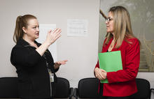 Congresswoman Jennifer Wexton in a red blazer, holding a green folder speaking with Mason faculty member Rebecca Sutter, wearing a black jacket. Rebecca is jestering with her hands while speaking with Honorable Wexton. 