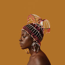 Orange brown background with an image of a Black woman with a beaded headdress by Carole Lee. The photographer is Kwame Brathwaite, ca 1969