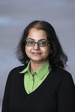 Soundararajan is wearing a green button up shirt under a black sweater, and wears glasses.