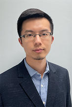 Yan is wearing glasses, a dark sportcoat and blue button up shirt