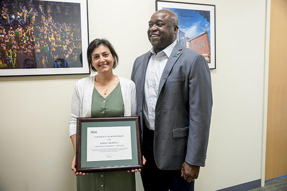 Maria Carabelli, right, holds her Employee of the Month certificate and stands next to Mason President Gregory Washington, left, in the corridor outside the President's Office.