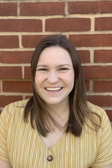 Headshot of Mason staff member Caroline Masakayan. She is smiling and standing in front of a brick wall.